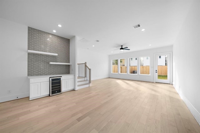 unfurnished living room featuring ceiling fan, bar, beverage cooler, and light hardwood / wood-style flooring