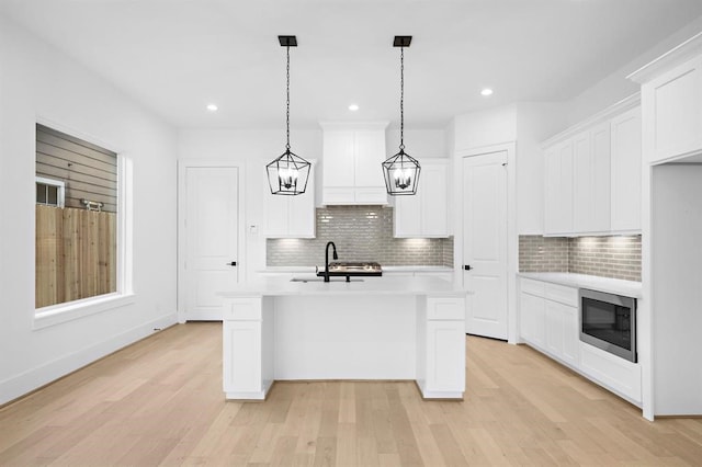 kitchen featuring pendant lighting, white cabinetry, an island with sink, built in microwave, and custom exhaust hood