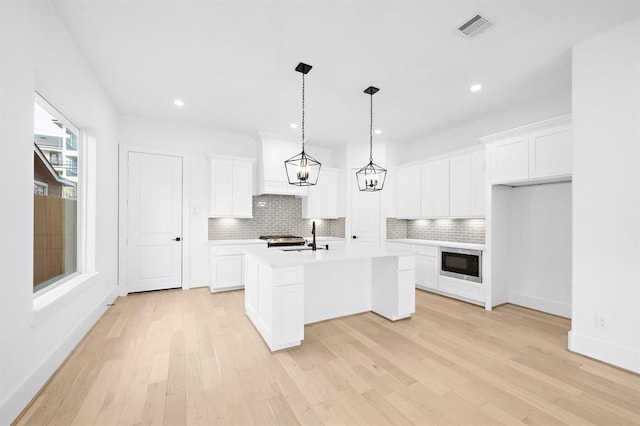 kitchen with white cabinetry, hanging light fixtures, built in microwave, and an island with sink