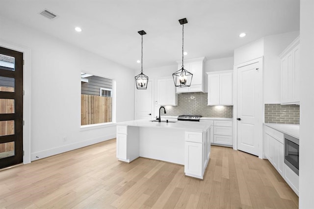 kitchen featuring an island with sink, white cabinets, and decorative light fixtures