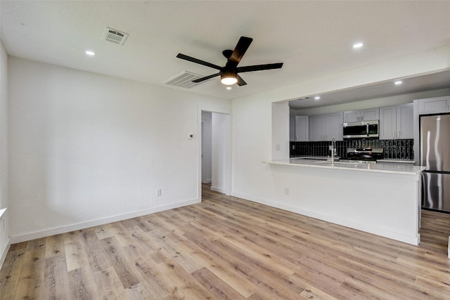 kitchen featuring ceiling fan, appliances with stainless steel finishes, decorative backsplash, kitchen peninsula, and light wood-type flooring