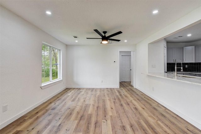 unfurnished living room with ceiling fan, sink, and light hardwood / wood-style flooring