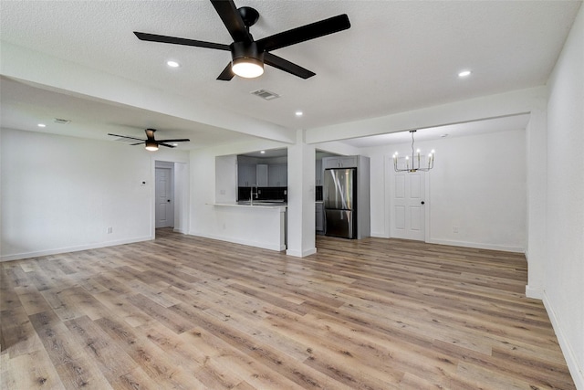 unfurnished living room featuring sink, ceiling fan with notable chandelier, a textured ceiling, and light wood-type flooring