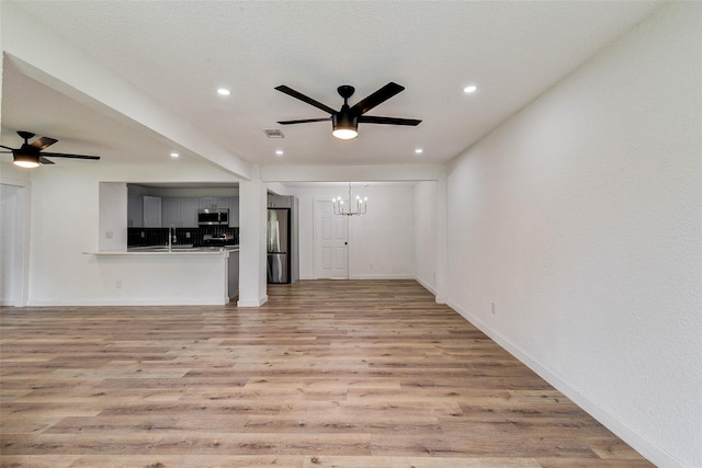 unfurnished living room with sink, ceiling fan with notable chandelier, light hardwood / wood-style flooring, and a textured ceiling