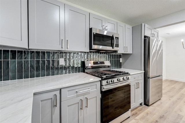 kitchen featuring appliances with stainless steel finishes, tasteful backsplash, light stone countertops, light hardwood / wood-style floors, and a textured ceiling