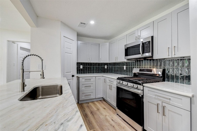 kitchen featuring tasteful backsplash, sink, light stone counters, light hardwood / wood-style floors, and stainless steel appliances