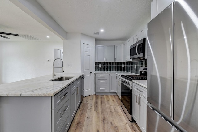 kitchen with sink, tasteful backsplash, light wood-type flooring, gray cabinets, and stainless steel appliances