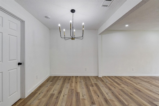 unfurnished dining area featuring an inviting chandelier, wood-type flooring, and a textured ceiling