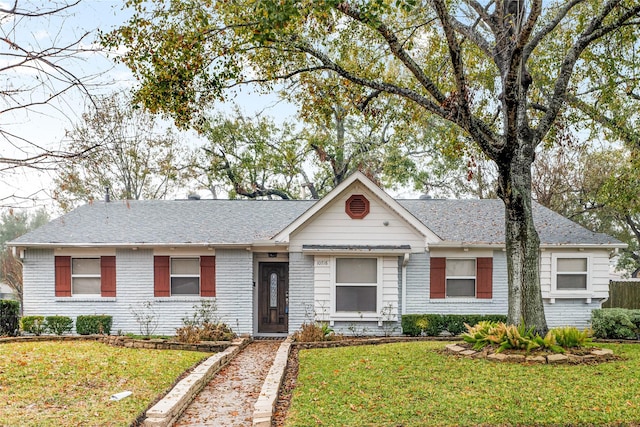 ranch-style home with a front lawn, roof with shingles, and brick siding