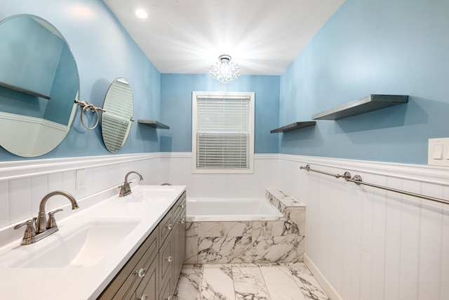 bathroom featuring a notable chandelier, vanity, and tiled tub