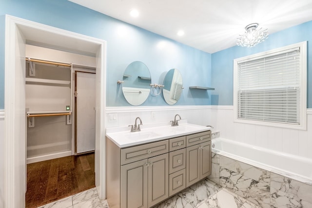 bathroom featuring vanity, tiled tub, and an inviting chandelier