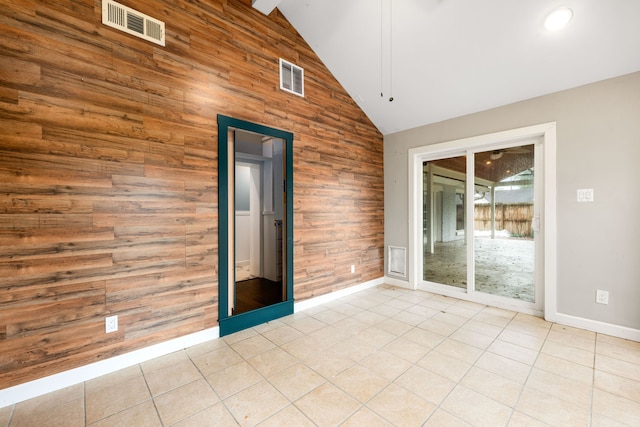 spare room with wooden walls, baseboards, visible vents, tile patterned floors, and high vaulted ceiling