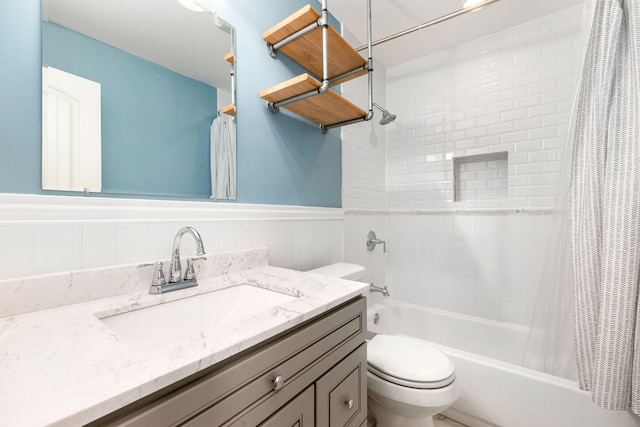 bathroom with a wainscoted wall, vanity, shower / bath combination with curtain, and toilet