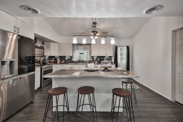 kitchen with stainless steel appliances, vaulted ceiling, a kitchen island, and white cabinets