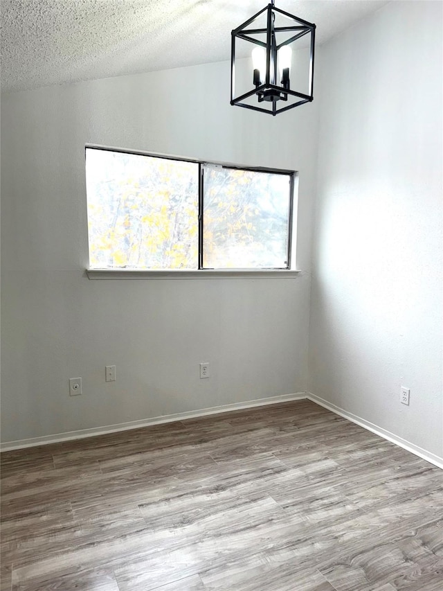 spare room with light hardwood / wood-style flooring, a chandelier, and a textured ceiling