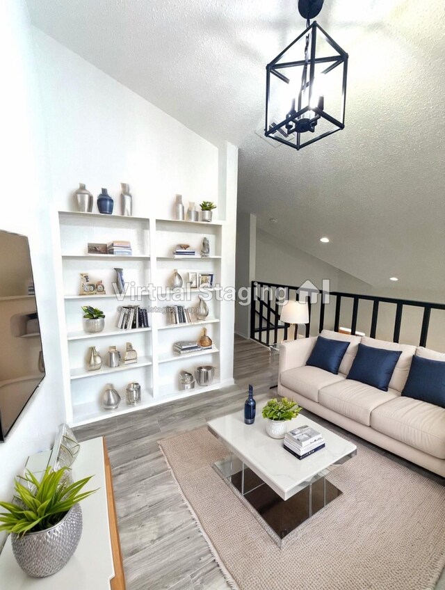 living room featuring wood-type flooring, lofted ceiling, a notable chandelier, and a textured ceiling