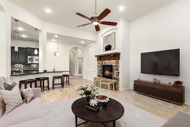 living room with crown molding, ceiling fan, a stone fireplace, and light hardwood / wood-style floors