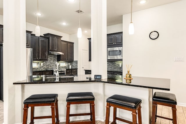 kitchen featuring tasteful backsplash, hanging light fixtures, stainless steel appliances, and kitchen peninsula