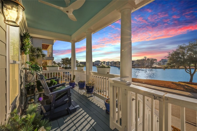 deck at dusk with a water view and ceiling fan