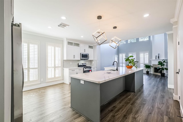 kitchen featuring appliances with stainless steel finishes, white cabinetry, hanging light fixtures, a kitchen island with sink, and decorative backsplash