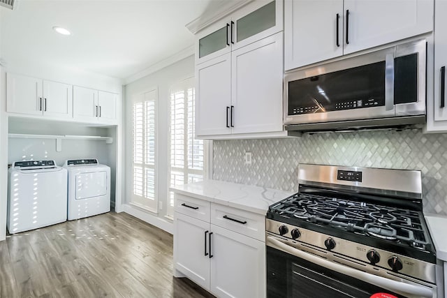 kitchen featuring appliances with stainless steel finishes, light stone counters, ornamental molding, washer and dryer, and white cabinets