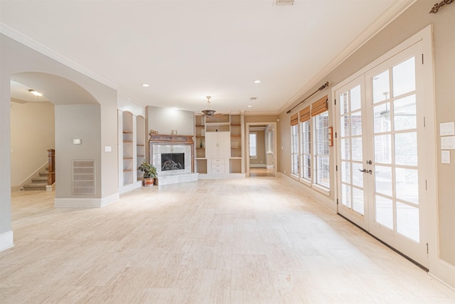 unfurnished living room featuring crown molding, built in shelves, and french doors