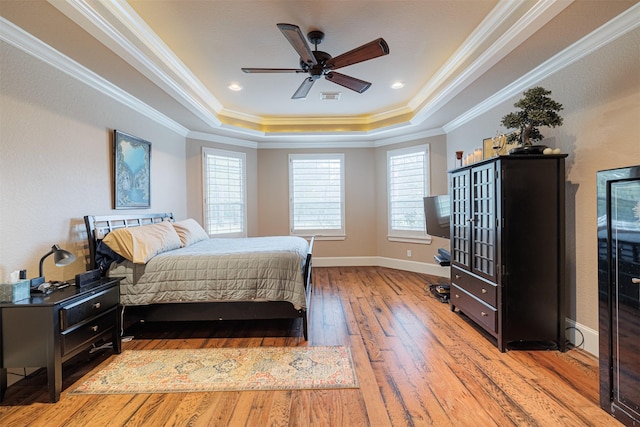 bedroom featuring light hardwood / wood-style flooring, ornamental molding, a raised ceiling, and ceiling fan