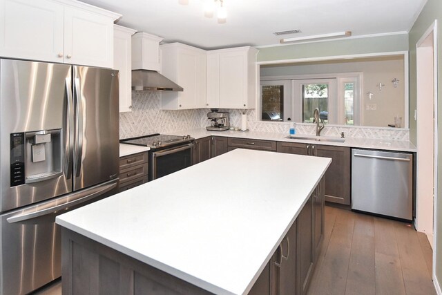 kitchen featuring appliances with stainless steel finishes, sink, white cabinets, a center island, and wall chimney range hood