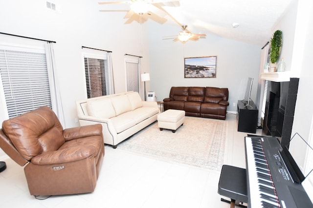 living room with ceiling fan, vaulted ceiling, and a tile fireplace