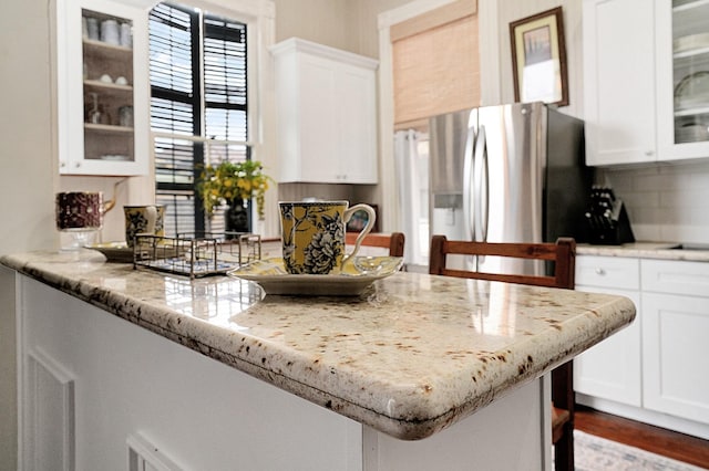 kitchen with stainless steel fridge, light stone countertops, white cabinets, and decorative backsplash