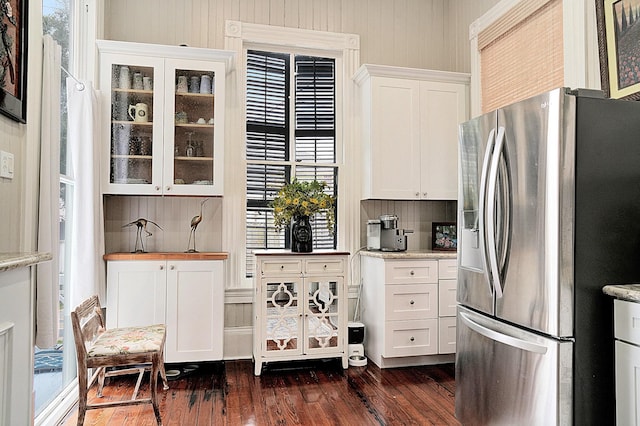 kitchen with stainless steel fridge, dark wood-type flooring, white cabinetry, backsplash, and light stone counters