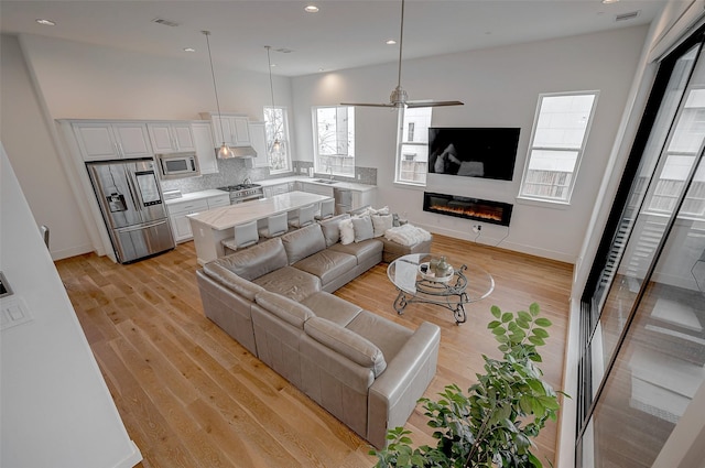 living room with ceiling fan, plenty of natural light, sink, and light wood-type flooring