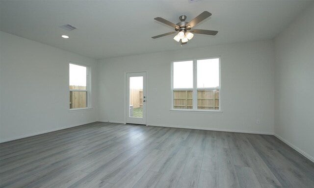 empty room with visible vents, ceiling fan, wood finished floors, and a healthy amount of sunlight