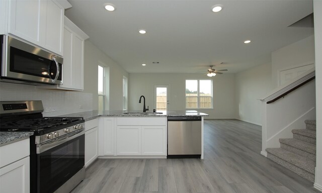 kitchen with a peninsula, white cabinetry, decorative backsplash, stainless steel appliances, and a sink
