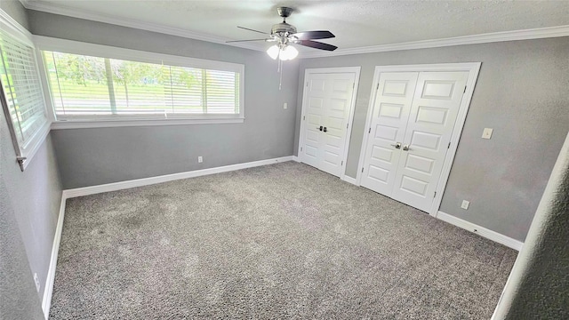 unfurnished bedroom with ornamental molding, carpet, ceiling fan, multiple closets, and a textured ceiling