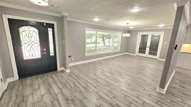 entrance foyer with ornamental molding, a textured ceiling, light wood-type flooring, and french doors