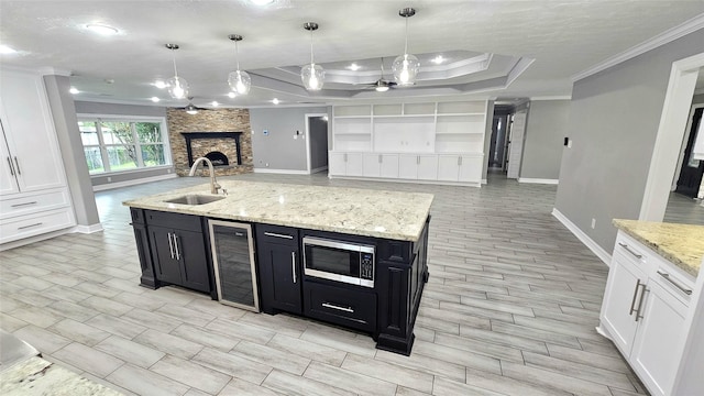 kitchen with wine cooler, sink, white cabinetry, stainless steel microwave, and pendant lighting