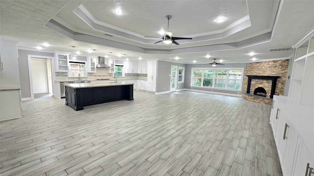 unfurnished living room with sink, ornamental molding, a tray ceiling, ceiling fan, and a fireplace