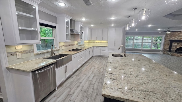 kitchen with pendant lighting, sink, appliances with stainless steel finishes, white cabinetry, and wall chimney exhaust hood