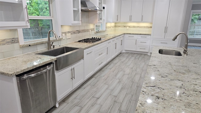 kitchen featuring sink, wall chimney range hood, white cabinets, and appliances with stainless steel finishes