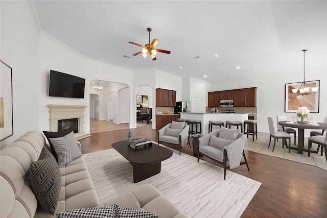 living room with crown molding, ceiling fan with notable chandelier, high vaulted ceiling, and light hardwood / wood-style flooring