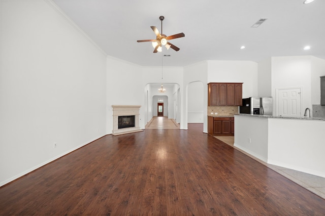 unfurnished living room featuring dark wood-type flooring, ceiling fan, crown molding, and sink