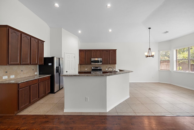 kitchen with appliances with stainless steel finishes, pendant lighting, light tile patterned floors, and dark stone counters