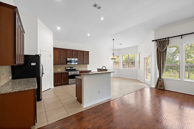 kitchen with backsplash, a chandelier, hanging light fixtures, light stone counters, and stainless steel appliances