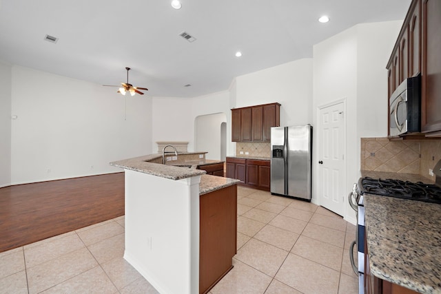 kitchen with appliances with stainless steel finishes, a kitchen island with sink, light tile patterned floors, ceiling fan, and light stone countertops