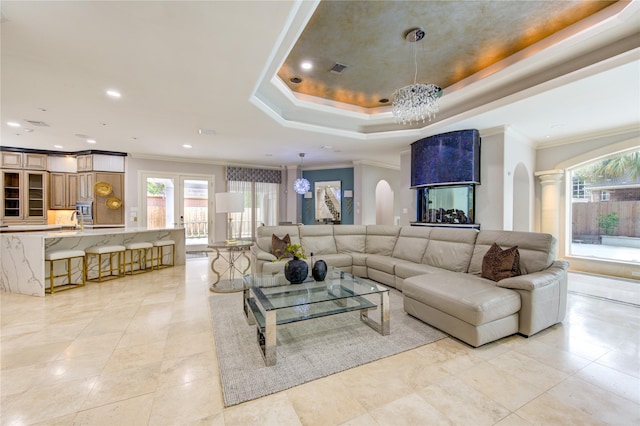 living room with ornamental molding, sink, an inviting chandelier, and a tray ceiling