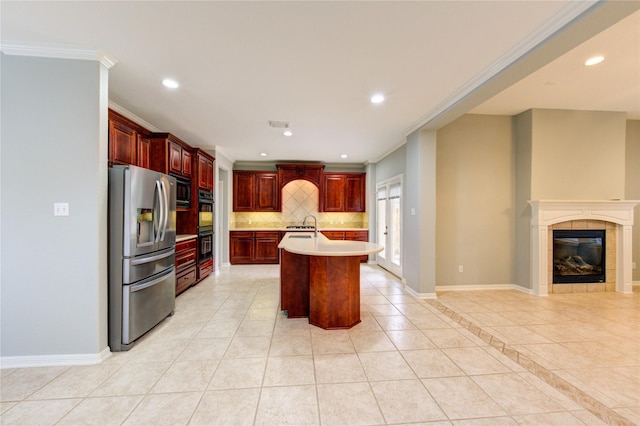 kitchen featuring an island with sink, backsplash, a tiled fireplace, ornamental molding, and black appliances