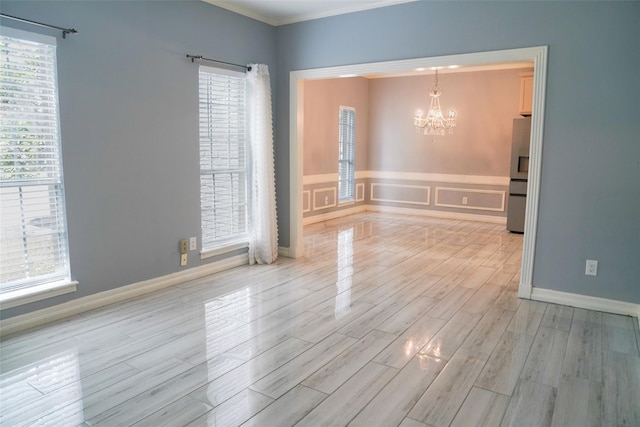 spare room with an inviting chandelier, a wealth of natural light, and light wood-type flooring