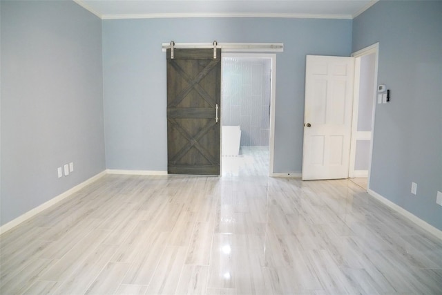 empty room with light hardwood / wood-style flooring, ornamental molding, and a barn door