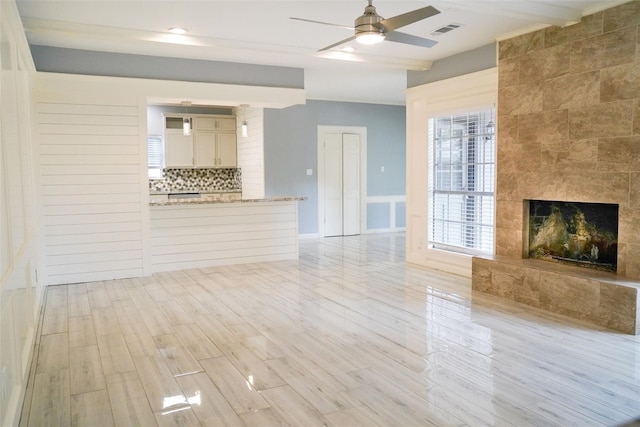 unfurnished living room featuring beamed ceiling, ceiling fan, a fireplace, and light hardwood / wood-style flooring